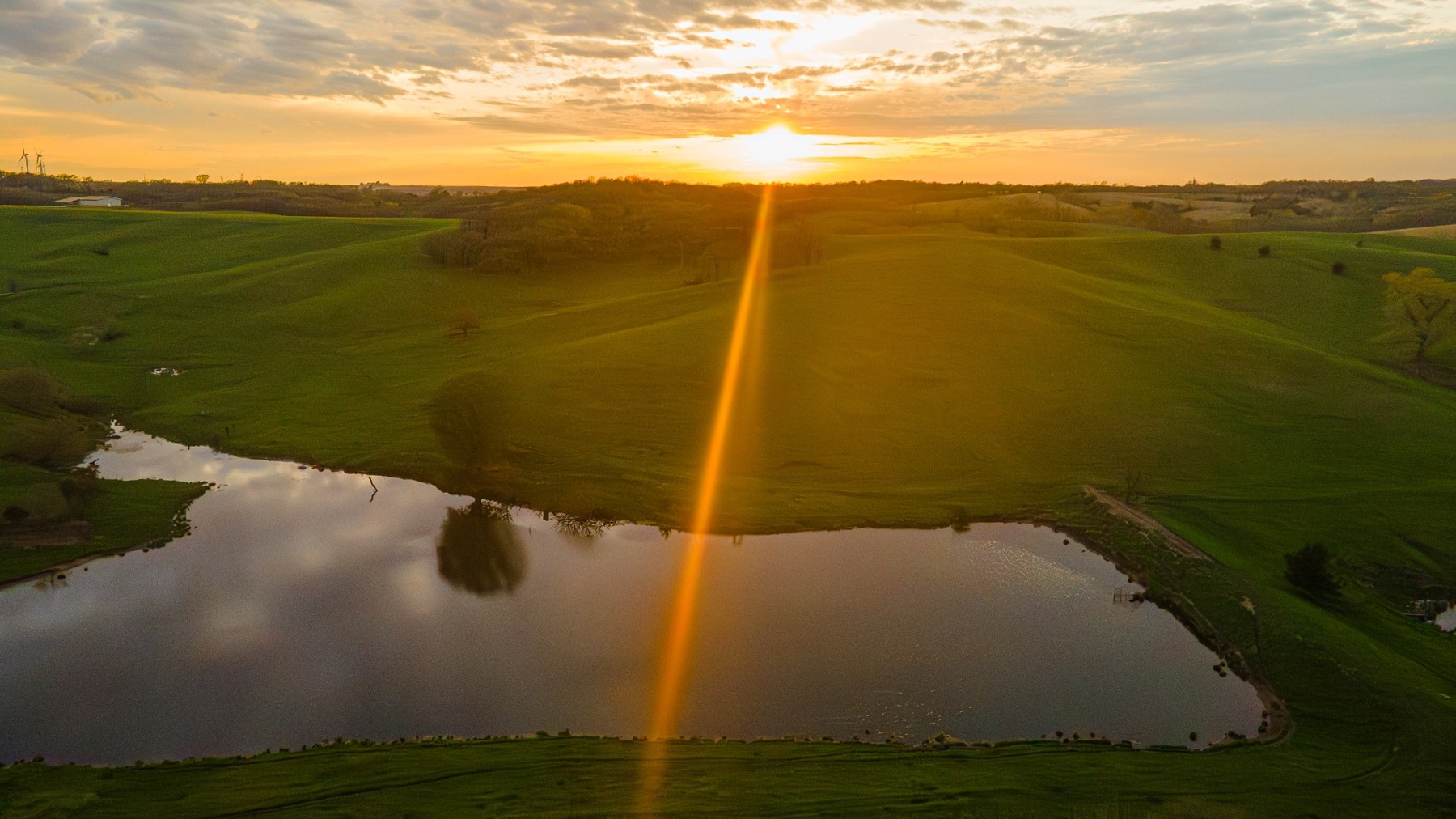 Aerial drone scenery photo of a sunset over rolling green Iowa land and a pond